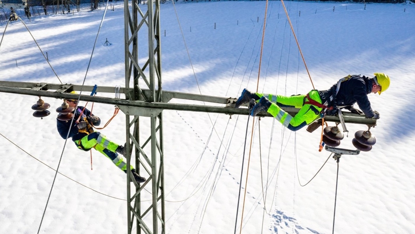 Zwei Monteure arbeiten an einem Hochspannungsmast im Schnee.