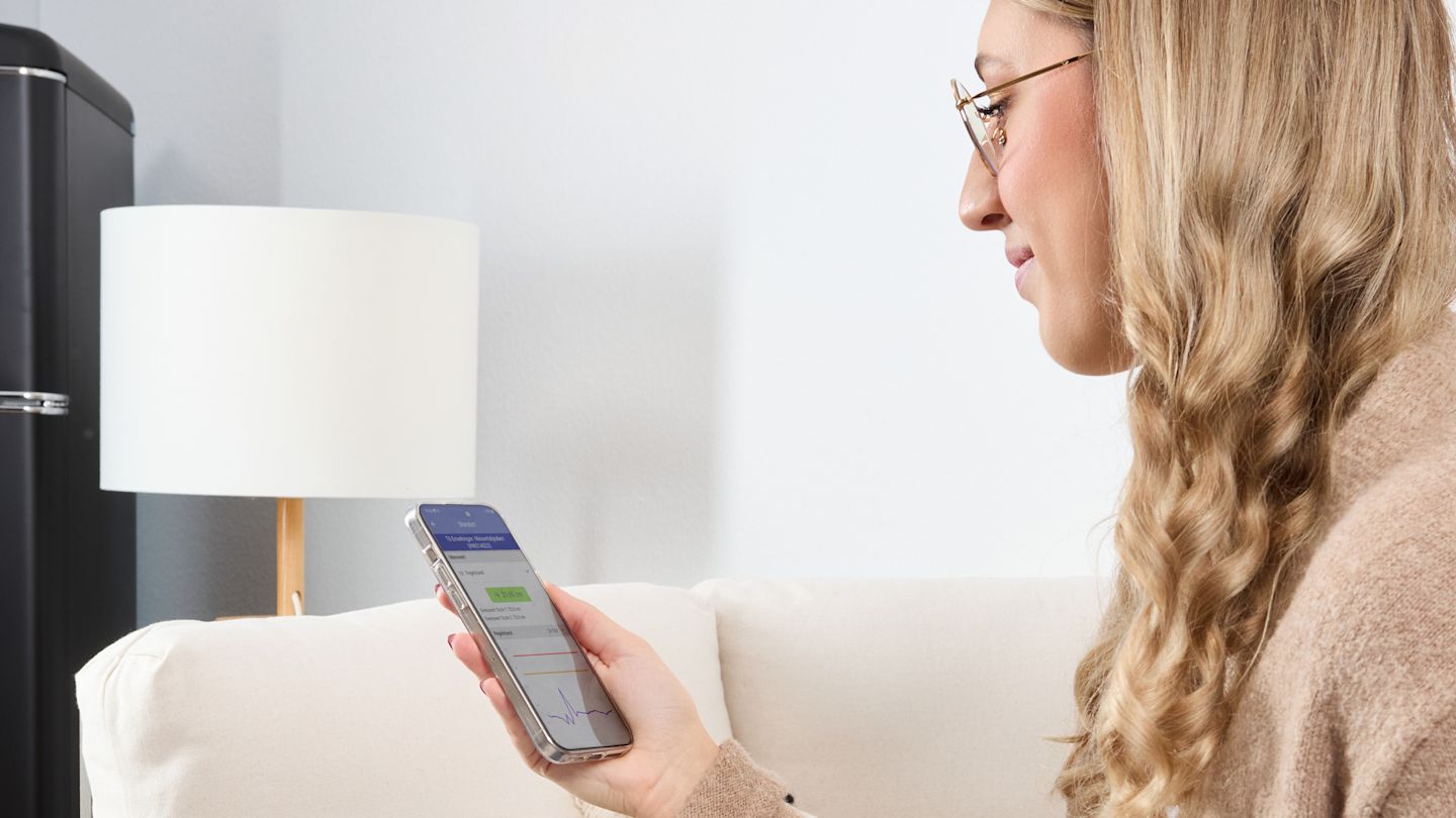 Frau sitzt auf dem Sofa und blickt zufrieden in ihr Smartphone.