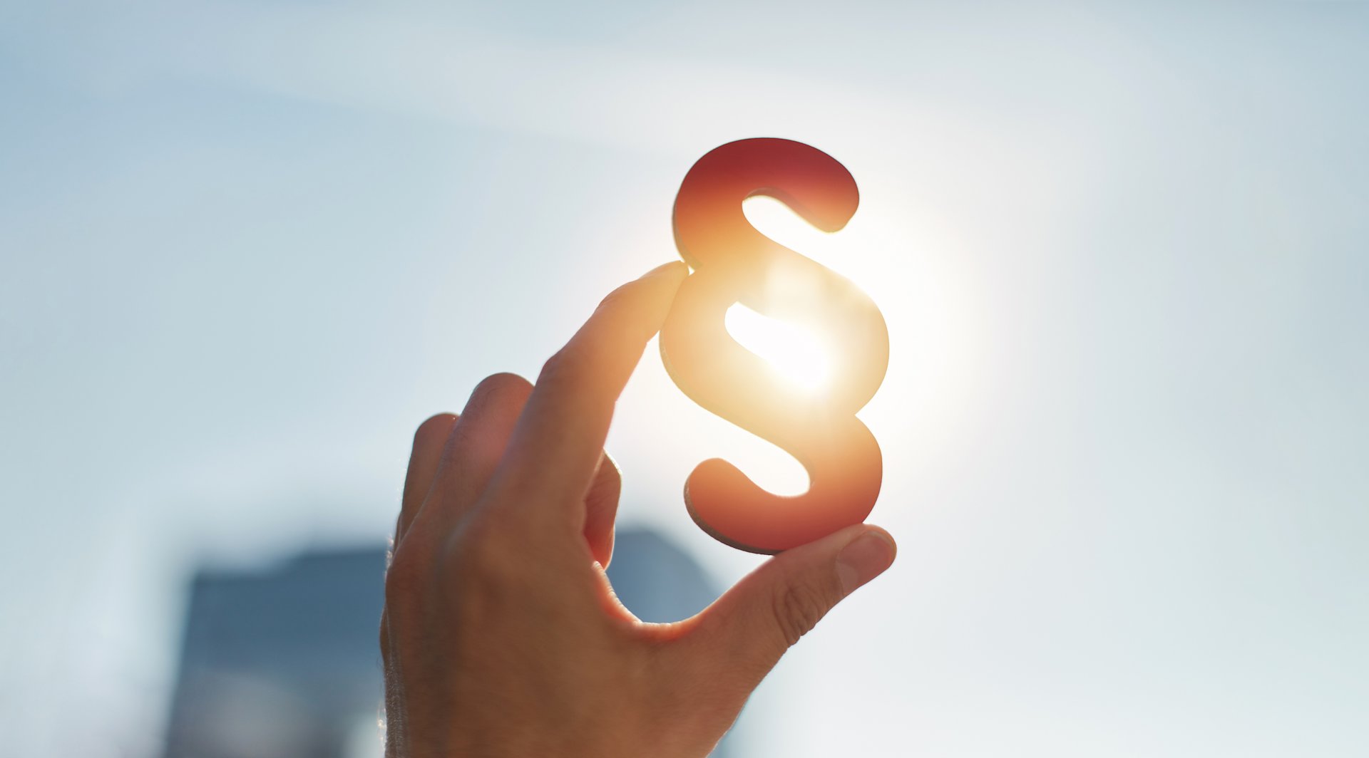 Eine Hand hält ein Paragrafzeichen gegen die Sonne.