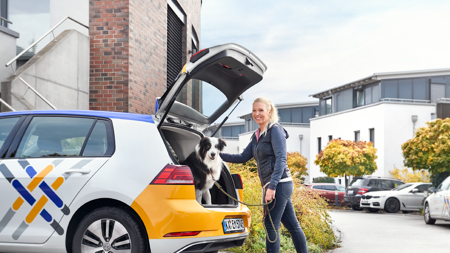 Anja Ziegler steht hinter einem E-Auto mit Hund im offenen Kofferraum.