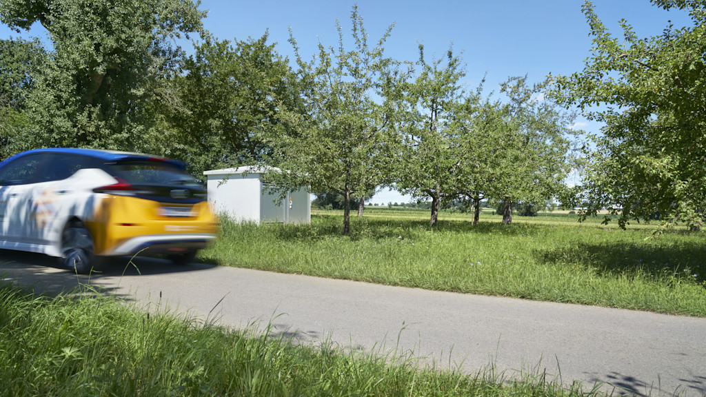 Auto fährt auf einer Landstraße zwischen zwei Wiesen vorbei.