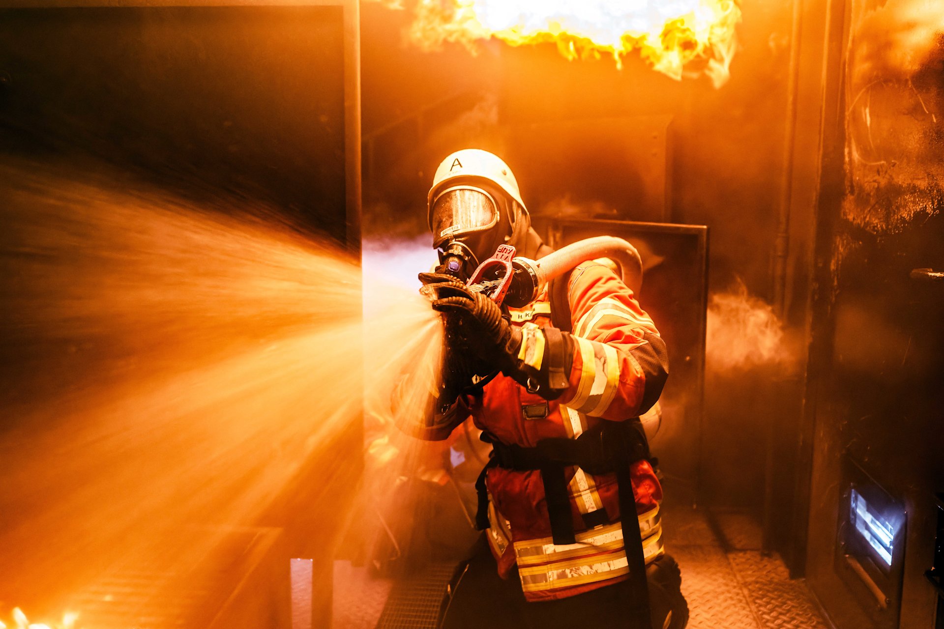 Feuerwehrmann mit Schlauch vor Flammen.
