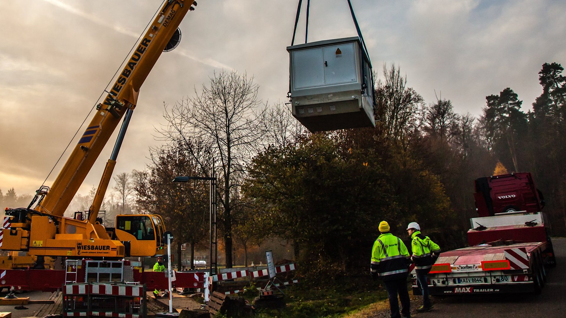 Kran liefert Trafostation auf Baustelle.